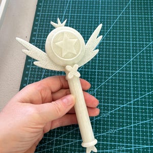 May include: A white plastic wand with a star-shaped top and wings. The wand is about 10 inches long and has a detailed design.