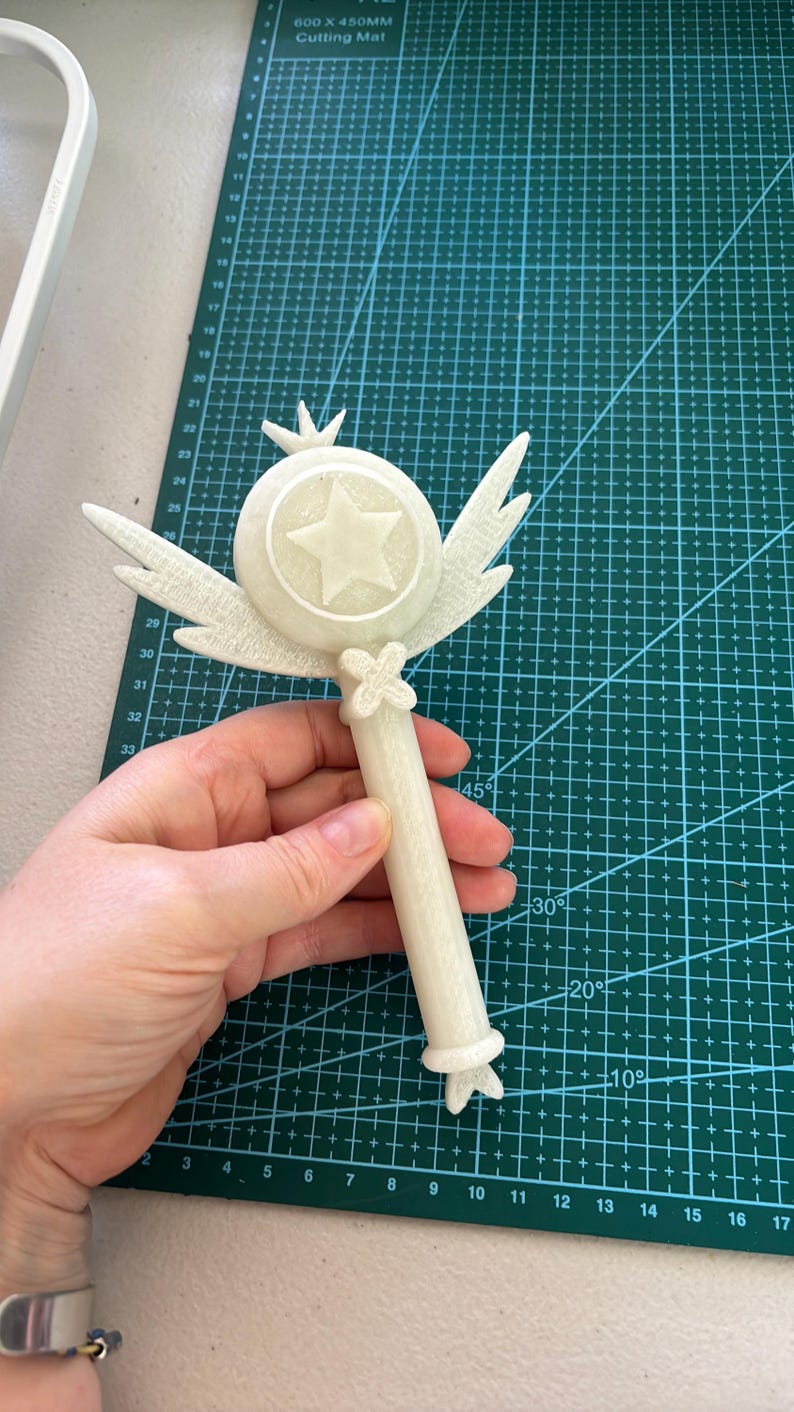 May include: A white plastic wand with a star-shaped top and wings. The wand is about 10 inches long and has a detailed design.