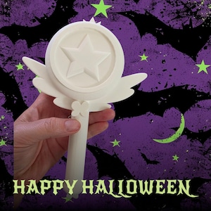 May include: A white plastic wand featuring a circular top with a raised star in the centre, flanked by two stylised wings on either side. The handle is cylindrical and includes a small butterfly-shaped detail where it meets the circular head.