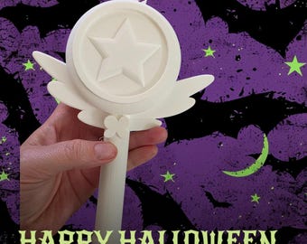 May include: A white plastic wand featuring a circular top with a raised star in the center, flanked by two stylized wings on either side. The handle is cylindrical and includes a small butterfly-shaped detail where it meets the circular head.