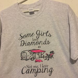 May include: Gray t-shirt with a black graphic that says "Some girls love diamonds. Not me, I love camping." The graphic also includes a cartoon of a camper, a woman sitting in a chair, and a cat.