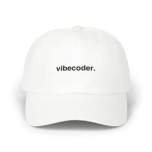 Puede incluir: Una gorra de béisbol blanca con el texto "vibecoder." bordado en hilo negro en el centro de la parte frontal. La gorra tiene una corona estructurada, una visera curva y un botón en la parte superior, presentando un diseño limpio y sencillo.