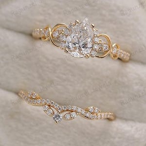 Può includere: Un set di anelli di fidanzamento in oro con un diamante a forma di pera e una fascia delicata. Il set include una fede nuziale curva abbinata, il tutto presentato in un portagioie di velluto.
