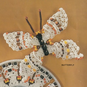 May include: A white crocheted butterfly with brown and yellow beads. The butterfly has pipe cleaner antennae and the word "BUTTERFLY" is written below it.
