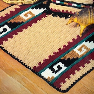 May include: A crocheted rug with a Southwestern design. The rug features a central tan field bordered by stripes of burgundy, black, teal, white, and brown. The design includes geometric patterns. An armadillo figurine rests on the rug.