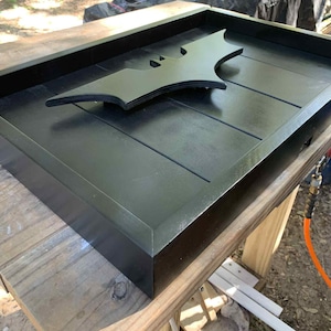 May include: A rectangular black wooden tray featuring a raised black bat-shaped emblem centered on the base. The tray has a smooth, matte finish with clean, straight edges and a slatted bottom design, providing a flat surface for display or storage.