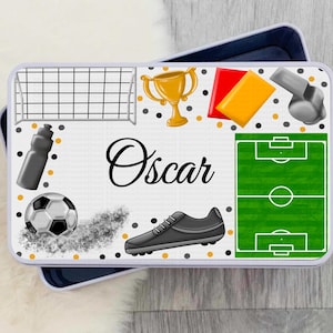 Könnte beinhalten: Weiße Metall-Lunchbox mit Fußball-Motiv. Sie zeigt einen Fußball, ein Tor, eine Pfeife, eine Trophäe, eine rote und gelbe Karte sowie einen Fußballplatz. Die Lunchbox ist mit dem Namen "Oscar" personalisiert.