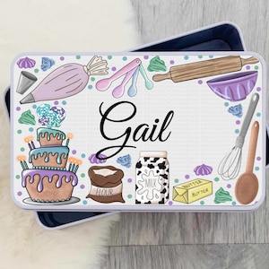 May include: A white rectangular tin with a colourful illustration of baking supplies, including a cake, a rolling pin, a bowl, and a bag of flour. The text "Gail" is written in black cursive lettering on the tin.