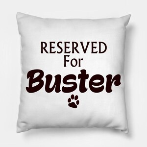 May include: White square cushion with the text "RESERVED For Buster" in dark brown, and a paw print. This pet-themed cushion is designed for a dog.