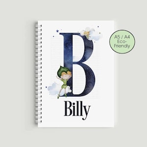 Könnte beinhalten: Ein weißes Spiralnotizbuch mit einem großen, marineblauen Buchstaben „B“ mit Sternenhimmel-Design. Eine Cartoonfigur und der Name „Billy“ sind ebenfalls auf dem Cover abgebildet. Das Notizbuch ist mit „A5 / A4 Eco-Friendly“ gekennzeichnet.