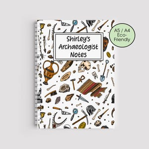 May include: A white spiral-bound notebook with a repeating pattern of colourful archaeological tools and artifacts. The notebook cover features the text "Shirley's Archaeologist Notes" and an "A5 / A4 Eco-Friendly" label.