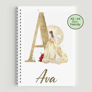 May include: A spiral-bound notebook featuring a gold-coloured letter 'A' and the name 'Ava' in gold script. The design includes a watercolour illustration of a woman in a yellow gown, a red rose, and a moon. The notebook has a green circle with the text 'A5 / A4 Eco-Friendly'.
