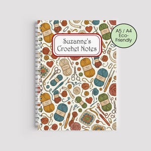 May include: A cream-coloured spiral-bound notebook with a pattern of crochet-related illustrations in various colours. The notebook features the text "Suzanne's Crochet Notes" in a red-bordered label. A green circle indicates the notebook is A5/A4 and eco-friendly.