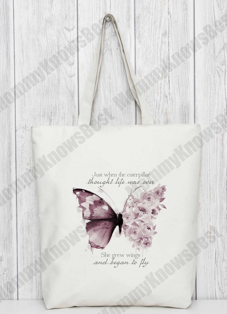 Pu&ograve; includere: Una borsa tote in tela bianca con una farfalla viola e un motivo floreale. La borsa ha il testo "Just when the caterpillar thought life was over she grew wings and began to fly."