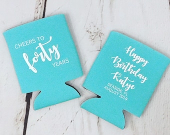Puede incluir: Dos enfriadores de latas de color azul turquesa con texto blanco. Un enfriador dice "Cheers to forty years" y el otro dice "Happy Birthday Katye Seaside, FL August 2019".