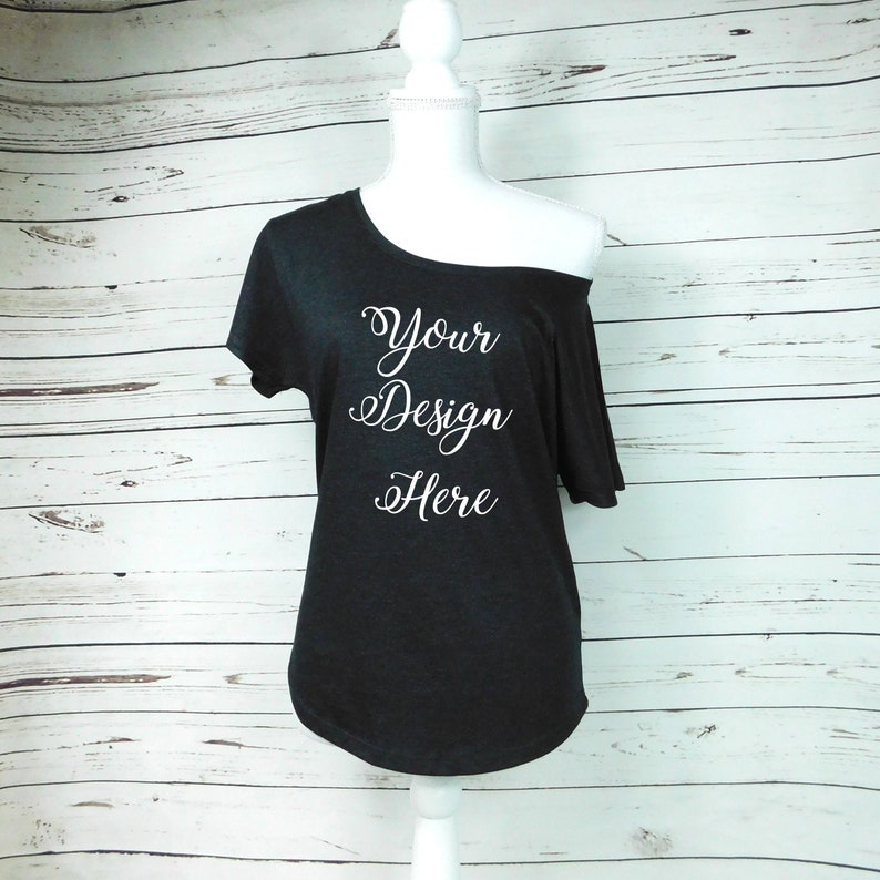 Op de afbeelding: Een zwart t-shirt met een off-shoulder ontwerp met de tekst "Your Design Here" in wit gedrukt op de voorkant.