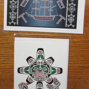 Może przedstawiać: Dwie kartki z życzeniami z motywem sztuki indiańskiej. Pierwsza kartka przedstawia statek z czerwonym kadłubem i białymi żaglami na niebieskim tle. Druga kartka przedstawia stylizowane zielono-czarne słońce z czerwonym otworem gęby i oczami oraz stylizowanego czarno-białego wieloryba. Kartka jest podpisana "David Bull".