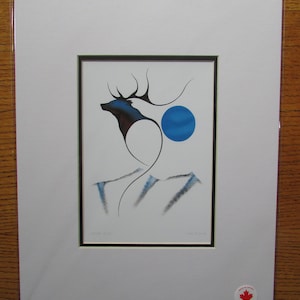 May include: A framed print of a stylized black and blue elk with a blue circle above it. The elk is standing on a white background with gray mountains in the background. The print is titled "Cedar Spirit" and signed by the artist.