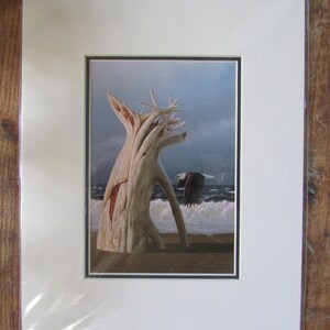 May include: A framed print of a painting depicting a weathered driftwood tree on a beach with a bald eagle flying overhead. The sky is cloudy and the ocean waves are crashing on the shore.