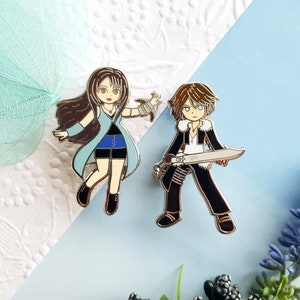 May include: Two enamel pins featuring characters from a popular video game. The female character is wearing a blue and white dress and has long brown hair. The male character is wearing a black jacket and pants and holding a sword. Both pins have a silver finish.