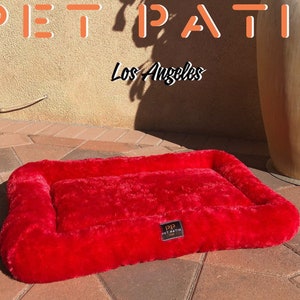 May include: A red plush dog bed with a raised edge and a "Pet Patio" logo. The bed is on a brick patio.