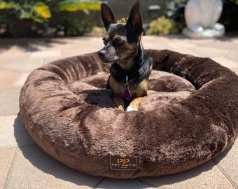 May include: A small brown dog bed with a brown fur-like texture. The bed has a raised edge and a logo that says "PP Pet Patio" in orange. A small black and brown chihuahua is sitting in the bed.