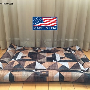 May include: A rectangular brown, black, and white geometric patterned dog bed with a raised edge. The bed has a label that reads "Pip Pet Patio". The bed is made in the USA.