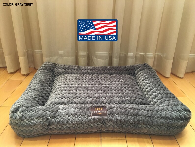 May include: Gray pet bed with a raised edge and a textured surface. The bed has a label that says "Pip Pet Patio" and "Made in USA".