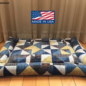 May include: A rectangular pet bed with a blue, yellow, and white geometric pattern. The bed has a raised edge and is made in the USA. The text "PIP PET PATIO" is visible on the bed.