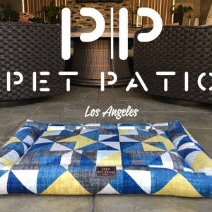 May include: A blue, yellow, and white geometric patterned dog bed with a "PIP PET PATIO Los Angeles" logo.