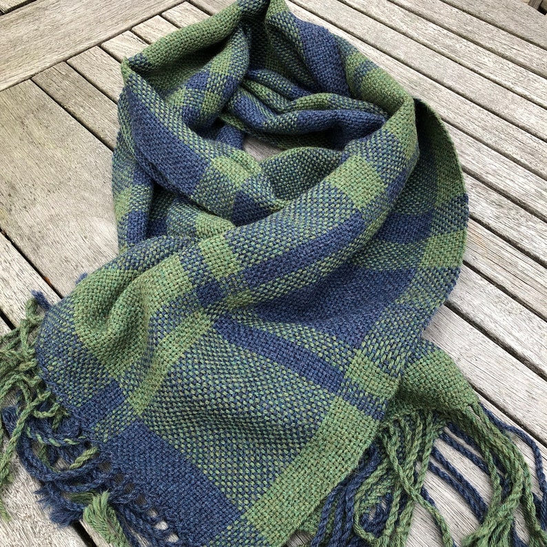 K&ouml;nnte beinhalten: Ein gr&uuml;n-blauer karierter Schal mit Fransen. Der Schal ist mit einem Karomuster gewebt.