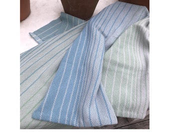 Könnte beinhalten: Drei Küchentücher in Grün-, Grau- und Blautönen mit einem gestreiften Muster. Die Tücher sind gefaltet und auf einer Holzoberfläche angeordnet. Der Text "Fog City Towels: Rigid Heddle version" ist in der rechten unteren Ecke sichtbar.