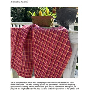 May include: A burgundy and gold woven towel with a grid pattern is draped over a white surface. The towel is made of cotton/linen blend. The text "Shadow Grid Towels" is visible at the top of the image.