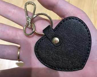 May include: A black leather heart-shaped keychain with a gold metal ring and clasp.