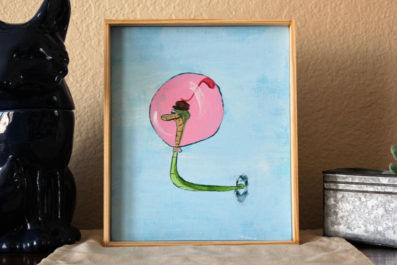 May include: A painting of a green snake with a brown hat inside a pink bubble on a light blue background.
