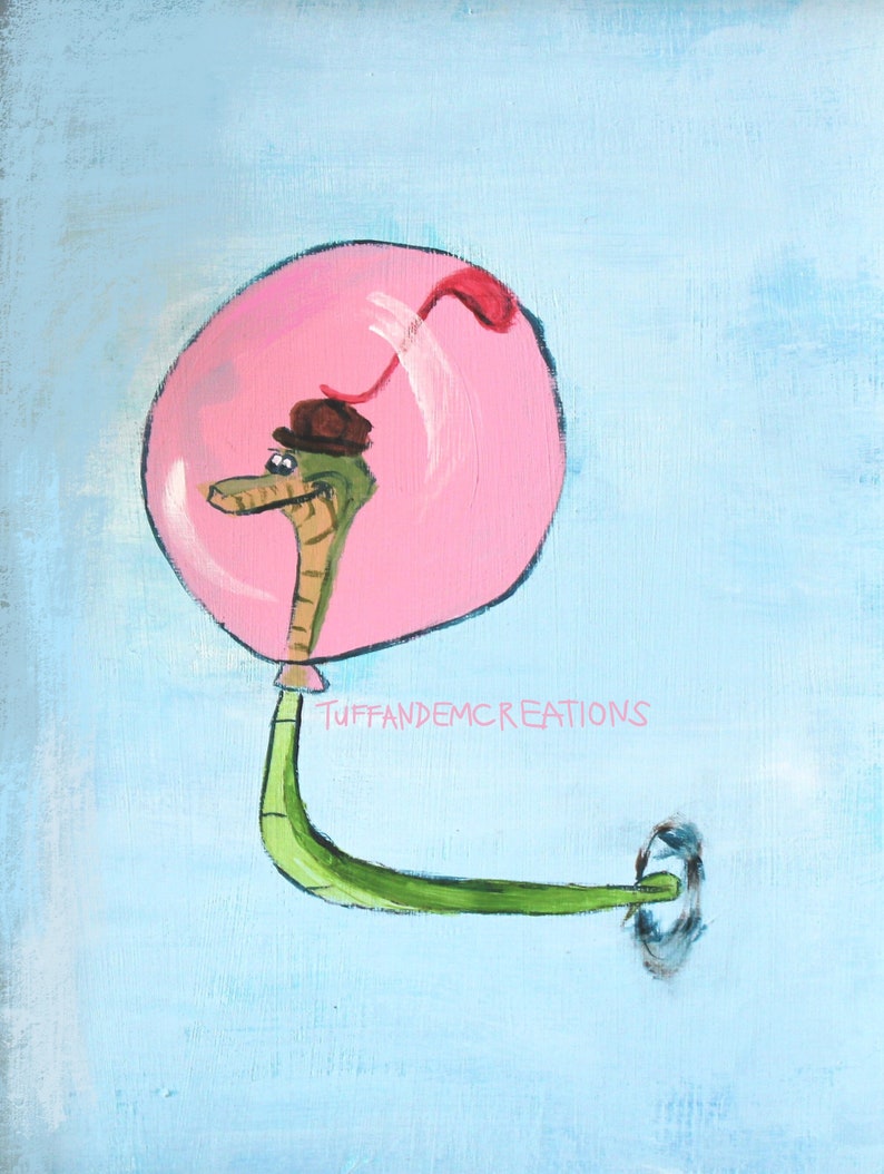 May include: A green snake wearing a brown hat floats in a pink bubble with a red tail. The snake is facing left and has a small, black eye. The background is a light blue colour. The text "TUFFANDEMCREATIONS" is written in black below the bubble.