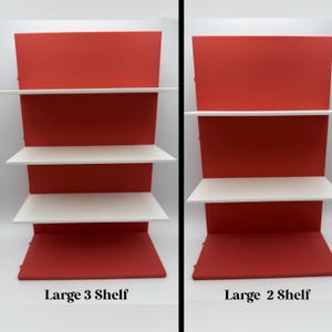 May include: Two display shelves, one with three white shelves and the other with two. Both have a red backing and base. The text "Large 3 Shelf" and "Large 2 Shelf" are at the bottom of each display.