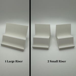 May include: Three white display risers. One large riser and two small risers are shown. The risers have a stepped design, with a flat base and a slightly angled top surface. The text "1 Large Riser" and "2 Small Riser" is below the risers.
