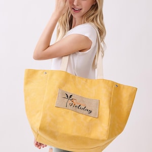 May include: A large yellow tote bag with two cream-colored fabric handles and a rectangular beige burlap patch on the front. The patch features a black palm tree graphic and the text "Summer Holiday" in a cursive black font with orange accents.