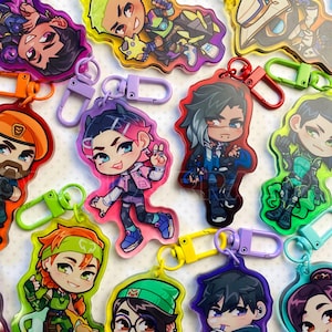 Puede incluir: Una colección de llaveros acrílicos coloridos con personajes de dibujos animados. Cada llavero tiene un diseño único con colores vibrantes y cierres metálicos. Los llaveros son de varias formas y tamaños, mostrando diferentes personajes.