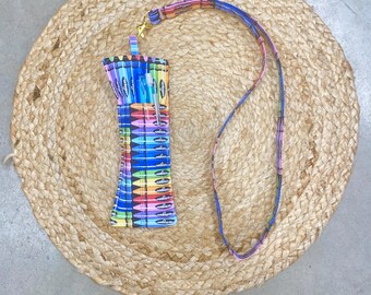 May include: A colorful crayon-themed lanyard with a matching holder. The holder is a rectangular shape with a rainbow crayon pattern. The lanyard and holder are on a woven, circular mat.