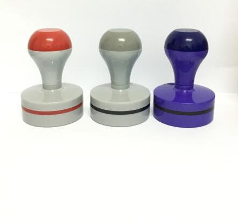 May include: Three rubber stamps with different colored tops: red, gray, and blue. Each stamp has a black base and a black ring around the top.