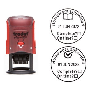 Op de afbeelding: Een rode zelf-inktende stempel met de tekst "trodat piinty 46130" en een zwarte handgreep. De stempel maakt een ronde afdruk met de tekst "Homework submitted 01 JUN 2022 Complete? On time?" en een vinkje of een open boekpictogram.
