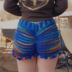 Può includere: Shorts in crochet blu e arancio con orlo a balze e pompon.