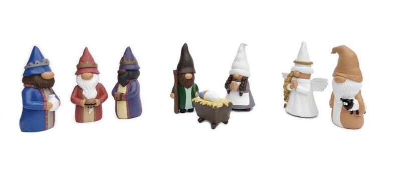 May include: A collection of ceramic Christmas gnomes in various colors. The set includes gnomes dressed as the three wise men, an angel, a shepherd with a sheep, and a gnome with a baby in a manger. The figures have detailed features and are set against a white background.