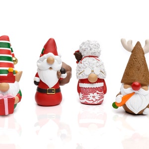 K&ouml;nnte beinhalten: Vier Weihnachtszwerg-Figuren. Die Zwerge tragen verschiedene festliche Outfits, darunter ein Elf, der Weihnachtsmann, Frau Claus und ein Rentier. Der Elf h&auml;lt ein Geschenk, der Weihnachtsmann tr&auml;gt einen Sack und das Rentier hat eine Karotte. Jeder Zwerg hat einen wei&szlig;en Bart.