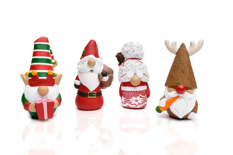 K&ouml;nnte beinhalten: Vier Weihnachtszwerg-Figuren. Die Zwerge tragen verschiedene festliche Outfits, darunter ein Elf, der Weihnachtsmann, Frau Claus und ein Rentier. Der Elf h&auml;lt ein Geschenk, der Weihnachtsmann tr&auml;gt einen Sack und das Rentier hat eine Karotte. Jeder Zwerg hat einen wei&szlig;en Bart.