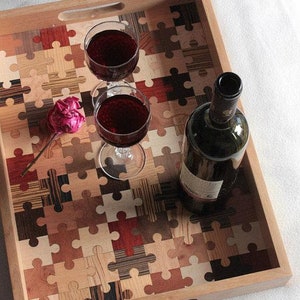K&ouml;nnte beinhalten: Ein Holztablett mit einem Puzzle-Design aus verschiedenen Holzarten. Das Tablett hat zwei Griffe und ist mit zwei Gl&auml;sern Rotwein und einer Flasche Rotwein gef&uuml;llt.