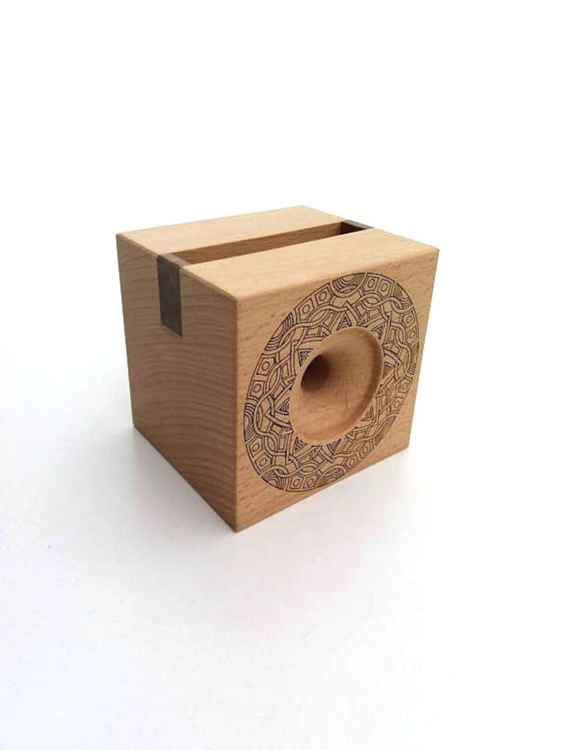 May include: A wooden phone stand with a geometric design carved into the front. The stand has a slot for holding a phone upright.