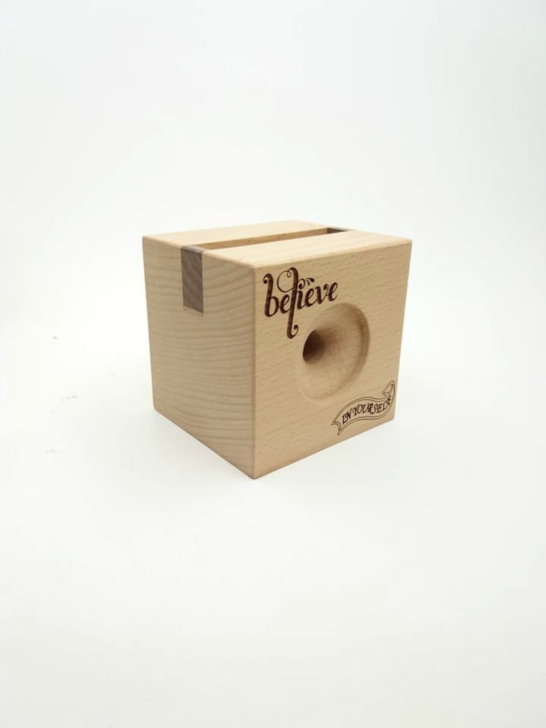 May include: A wooden phone stand with a cutout for a phone and the words "believe in your dream" engraved on the front.